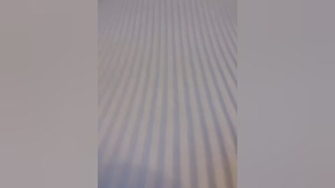 A video capturing a close-up view of a textured, wavy surface with vertical, parallel ridges. The surface appears smooth and slightly reflective, creating a subtle shimmer effect. The background is plain and neutral, enhancing the focus on the textured pattern.