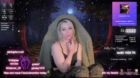 Media: A video of a blonde woman with fair skin, wearing a green blanket and black lingerie, sitting in a dimly lit, forested setting. She looks tired and pensive, with a text overlay displaying streaming information.