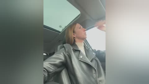 Media: A video shows a blonde woman in a gray leather jacket and white turtleneck leaning out of a car window, looking up at the sky.