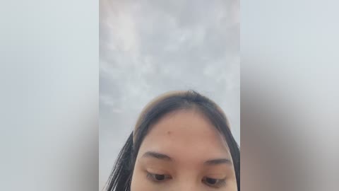 Media: Video of a young Asian woman with straight, dark hair, looking downwards, partially obscured by a dense, foggy background. Her smooth, fair skin and subtle makeup are visible.