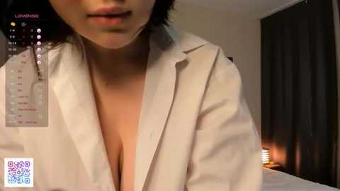 Media: A close-up video of an Asian woman with short black hair, partially open white shirt, revealing cleavage, in a dimly-lit bedroom with a calendar and QR code in the background.