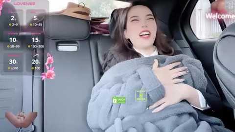 Media: Video of a smiling woman in a car, wrapped in a gray blanket, with a digital interface displaying temperature and location.