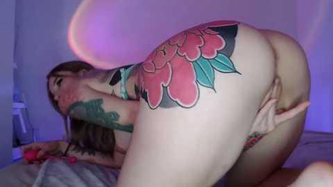 Media: Video of a nude, light-skinned woman with a large, colorful rose tattoo on her buttocks, positioned on all fours on a bed, in a dimly lit room.