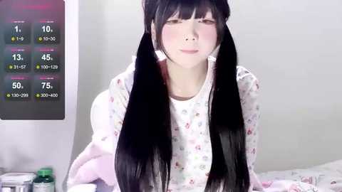 Media: Video of a young Asian woman with long black pigtails, wearing a floral-patterned pajama top, sitting on a bed. A digital thermometer and medicine bottle are visible on the bedside table.