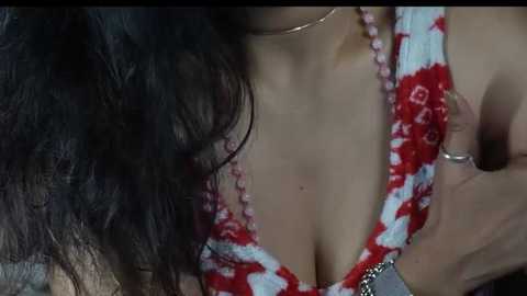 Media: Video of a woman with long, dark hair, wearing a red floral-patterned dress, exposing cleavage, with a man's hand on her breast, visible necklace.