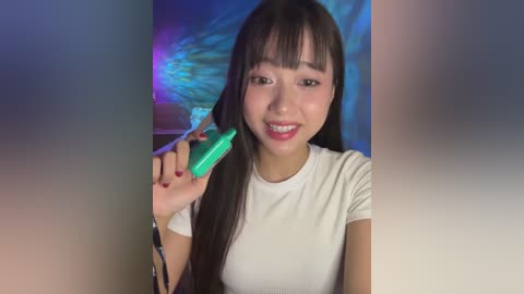 Media: Video of an Asian woman with long black hair, smiling, holding a green vape pen, wearing a white t-shirt, with a colorful, abstract background.