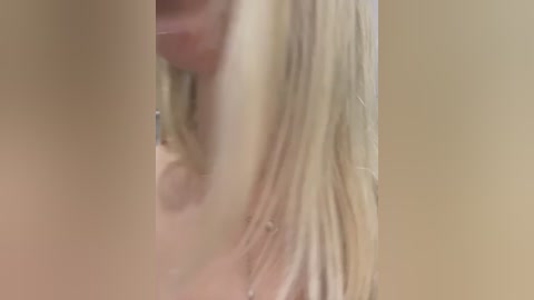 Media: A blurry video showing a close-up of a blonde woman's face and shoulder, with indistinct facial features and hair. The background is a plain, beige wall.