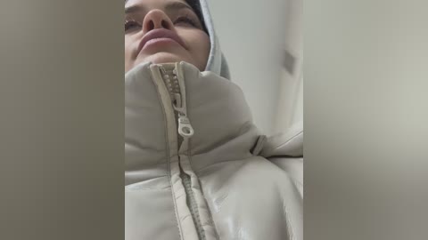 Media: Video of a person wearing a white, puffy winter coat with a hood, standing against a blurred background. The image focuses on the chest and face, showing a woman with a neutral expression and light skin tone.