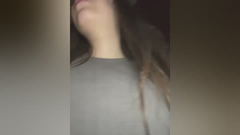 Media: A blurry video showing a partially visible person with long brown hair and a grey shirt. The background is dark and indistinct, with a focus on the upper body and head.