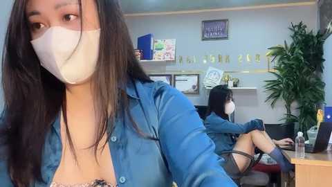 Media: Video of two Asian women in a modern office; one in blue denim shirt, white mask, and long black hair, the other in black dress, white mask, and short black hair.