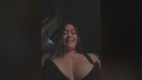 Media: Video of a smiling, light-skinned woman with shoulder-length brown hair wearing a black bra, captured in a dimly lit, cramped car interior.