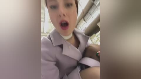 Media: A blurry video shows a woman with light skin, brown hair, and a white blouse, looking surprised, framed by a white window.