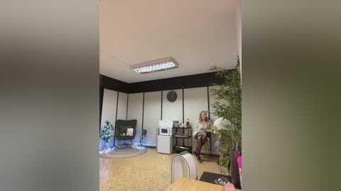 Media: A video of a modern office with a woman in a white blouse and black skirt sitting at a desk, a potted plant on the right, and a clock on the wall.