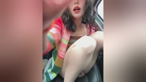 Media: A video of a woman with shoulder-length dark hair, wearing a colorful striped blanket, sitting in a car. Her face is partially visible, and her legs are crossed. The background includes car seats.