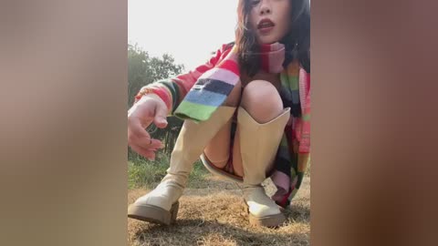 Media: A video of a woman squatting outdoors, wearing a colorful striped scarf, red plaid jacket, beige boots, and dark hair, against a blurred green background.