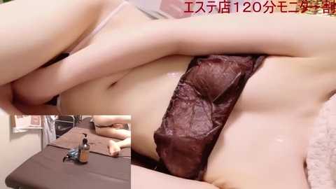 Media: A close-up video of a woman with fair skin and medium-sized breasts, wearing sheer black lingerie, partially obscured by her hands. A small toy figure is placed on a table beside her.