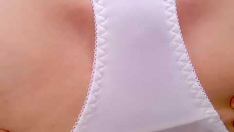 Media: Video of a woman's upper torso in a white, sheer lace bra, highlighting the soft texture and delicate stitching. The skin is smooth with a light, natural tan.