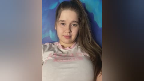 Media: Video of a young girl with light skin, long brown hair tied in a high ponytail, wearing a light pink blouse. Background features a blue and purple abstract painting.