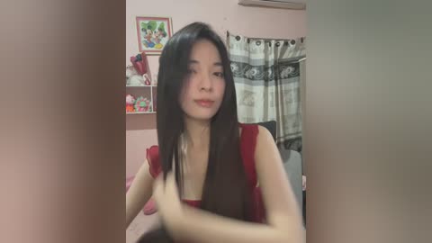 Media: A video of an Asian woman with long black hair, sitting in a pink room with a framed picture on the wall, holding her hair.