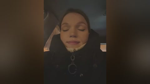 Media: A video of a woman with closed eyes, wearing a black jacket with a fur collar, sitting in a dimly lit car, creating a moody, intimate atmosphere.