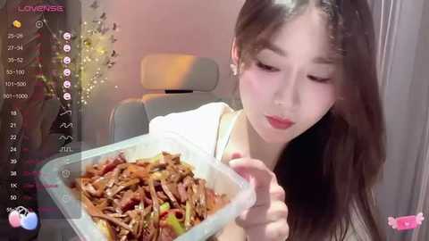 Media: A video of an East Asian woman with long black hair, wearing a white top, holding a clear container filled with cooked duck meat. The background features a modern, minimalist room with a grey chair.