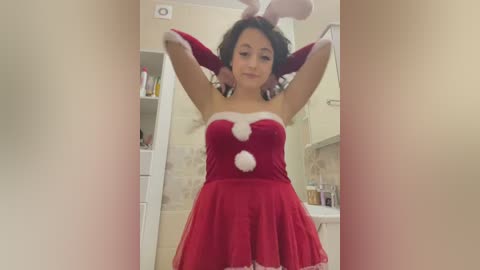 Media: Video of a young Asian woman with short black hair, wearing a festive red bunny costume with white fur trim, in a bathroom with beige tiles and toiletries.