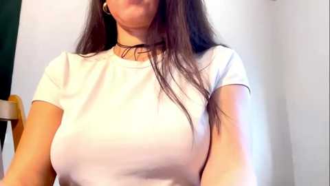 Media: A video of a young woman with long, dark hair, wearing a white t-shirt and a black choker, sitting against a plain, light-colored wall.