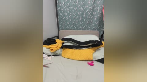 Media: Video of a messy bedroom with a bed covered in yellow and black blankets, a pink vibrator on the floor, and a floral-patterned wall.