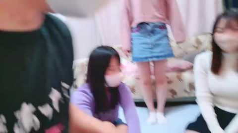 Media: Video of four people in a living room: two young women with long black hair in purple and white sweaters, one man in a dark shirt, and another woman in a pink sweater.