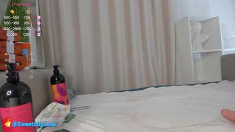 Media: A video of a hospital room with two black bottles, a blanket, and a person's hand on a white bed. The room has beige curtains and a white wall.