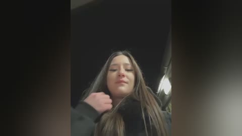 Media: A video of a young woman with long brown hair, wearing a black coat, sitting in a car, eyes closed, resting her head on her hand.