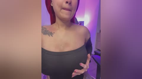 Media: Video of a woman with fair skin, red hair, and large breasts, wearing a black off-shoulder top, standing indoors with purple lighting, visible tattoo on shoulder.