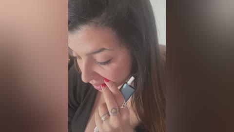 Media: Video of a young woman with long, dark hair, wearing a black cardigan and a white top, holding a cigarette to her lips, with a blurred background.