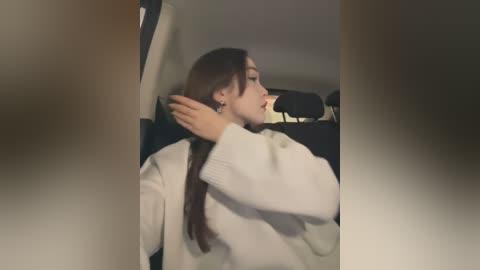 Media: Video of a young woman with long brown hair, wearing a white sweater, adjusting her hair in a car.