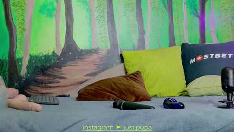 Media: A video of a cozy bedroom with a green forest mural on the wall, featuring a bed with pillows and a stuffed animal, a remote control, and a microphone.