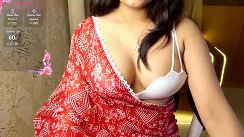 Media: Video of a South Asian woman with medium brown skin, wearing a white lace bra and red patterned sari, in an indoor setting.