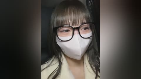 Media: Video of an East Asian woman with long black hair, wearing glasses, white mask, and beige coat, standing indoors with blurred background.