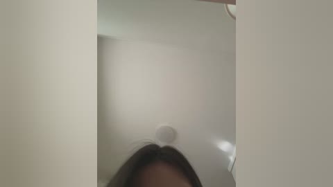 Media: A blurred video of a person with shoulder-length brown hair in a white room, standing in front of a mirror, capturing the reflection of the ceiling light and the person's face.