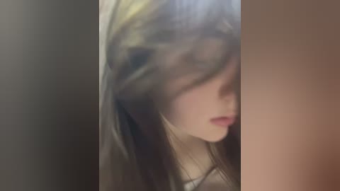 Media: Video of a young woman with long, wavy, brown hair partially covering her face, wearing a beige sweater. The background is a gradient of dark to light brown.