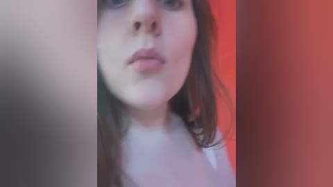 Media: A blurred video of a young woman with fair skin and long brown hair, partially visible in a dimly lit room with red and orange lighting.