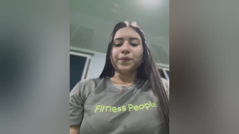 Media: Video of a young woman with long dark hair, wearing a grey t-shirt with \"Fitness People\" written on it. She has a light skin tone and a neutral expression.