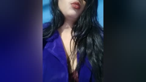 Media: Video of a woman with long, wet black hair, wearing a purple jacket over a red lace bra, against a blue background.