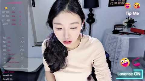 Media: Video of an East Asian woman with long black hair, fair skin, and a slender physique, wearing a beige top, looking down. Background shows a modern office with a desk, lamp, and calendar. Text overlay: \"Live ON\" with heart emojis.