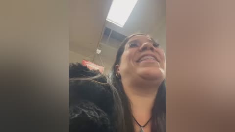 Media: A video of a smiling woman with long brown hair, wearing a black fur coat, standing indoors near a ceiling light.