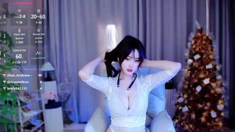 Media: Video of an Asian woman in a white lace dress, combing her hair with a black comb, in a dimly lit room with a Christmas tree, a bed, and a chair.