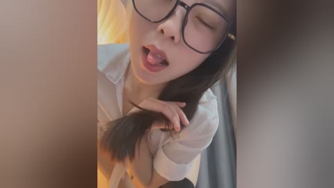 Media: A video of an Asian woman with long black hair, wearing glasses, playfully pulling her hair in a seductive manner. She is dressed in a white shirt and has a sensual expression.