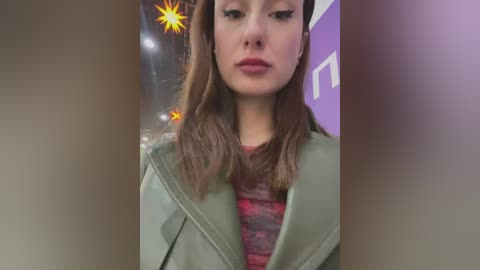 Media: A close-up video of a young woman with light skin, long brown hair, and wearing a green coat over a red sweater, against a purple wall with a starburst pattern.