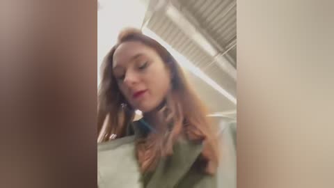 Media: A blurry video shows a young woman with light skin, long brown hair, and red lipstick, looking down. She's in a car with a beige interior and a corrugated metal ceiling.