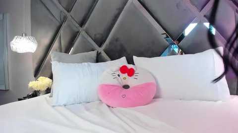 Media: Video of a modern bedroom featuring a plush white bed with a pink Hello Kitty pillow, diamond-patterned gray headboard, and a hanging crystal chandelier.