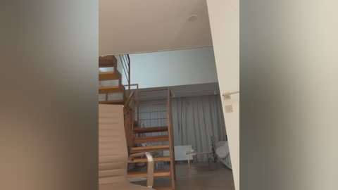 Media: Video of a modern, minimalist apartment with beige walls, a wooden staircase, and a white sofa against sheer white curtains.